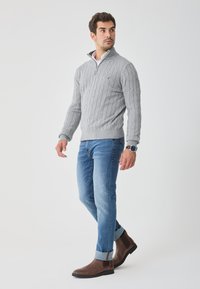 Maglione grigio a maglia con zip al colletto, abbinato a jeans azzurri e stivali alla caviglia in pelle marrone. Presenta maniche risvoltabili.
