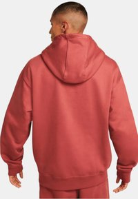 Röd bomullshuvtröja med en stor huva, sänkta axlar och ribbade ärmslut. Slät textur och avslappnad passform.