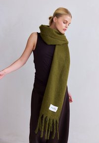 Écharpe en laine vert olive avec une finition texturée, des bords frangés et une étiquette blanche portant la mention "ARCTIC FOX" sur le bord inférieur.