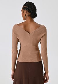 Brauner, gerippter, enganliegender Pullover mit V-Ausschnitt und langen Ärmeln, der ein strukturiertes Muster und gestaffelte Nähte auf der Rückseite aufweist.
