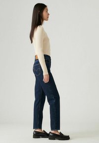 Geribbelde crème lange mouwen top gecombineerd met donkerblauwe rechte jeans. Zwarte loafers met een textuurafwerking maken de outfit compleet.