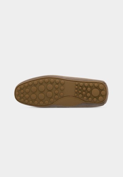 Semelle d'une chaussure marron avec des picots en caoutchouc ronds répartis uniformément pour offrir adhérence et traction, sur un fond gris neutre.