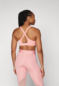 Brasile sportivo rosa con spalline incrociate e dettaglio a occhiello sulla schiena. Abbinato a leggings a vita alta coordinati con pannelli in rete.