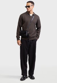 Pulover polo tricotat maro închis, geantă de umăr neagră, pantaloni negri cu croială largă, pantofi negri cu talpă groasă și ochelari de soare cu rame pătrate.