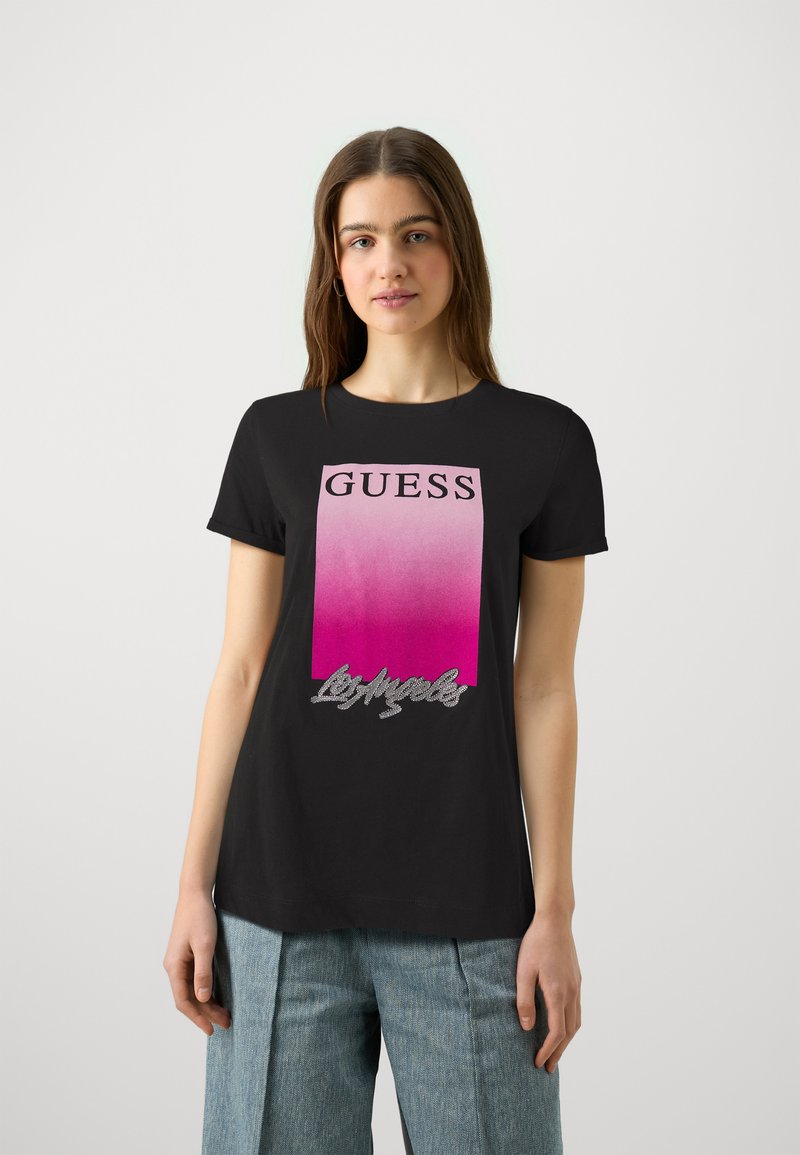 Zwarte t-shirt met een gradiënt roze en witte rechthoekige logo met "GUESS" in vetgedrukte zwarte letters en een decoratieve zilveren schrift eronder.