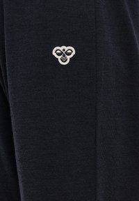 Zwarte textiel met een klein, geborduurd embleem in grijs en wit in de bovenlinkerkant, dat een gestileerd bijontwerp afgebeeldt.