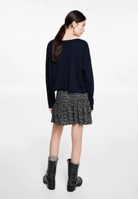 Schwarz-weiße gemusterte Minirock mit ausgestelltem Design, kombiniert mit einem übergroßen marineblauen Pullover und schwarzen Knöchelstiefeln mit dicken Sohlen.