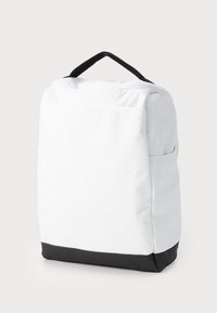 Mochila blanca con una superficie texturizada, fondo negro, cierre de cremallera y asa en la parte superior. Cuenta con un bolsillo lateral para almacenamiento adicional.