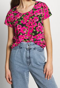 Kwiatowa bluzka z krótkim rękawem z jasnoróżowymi kwiatami na czarnym tle, zestawiona z jasnoniebieskimi dżinsami z wysokim stanem i paskiem.