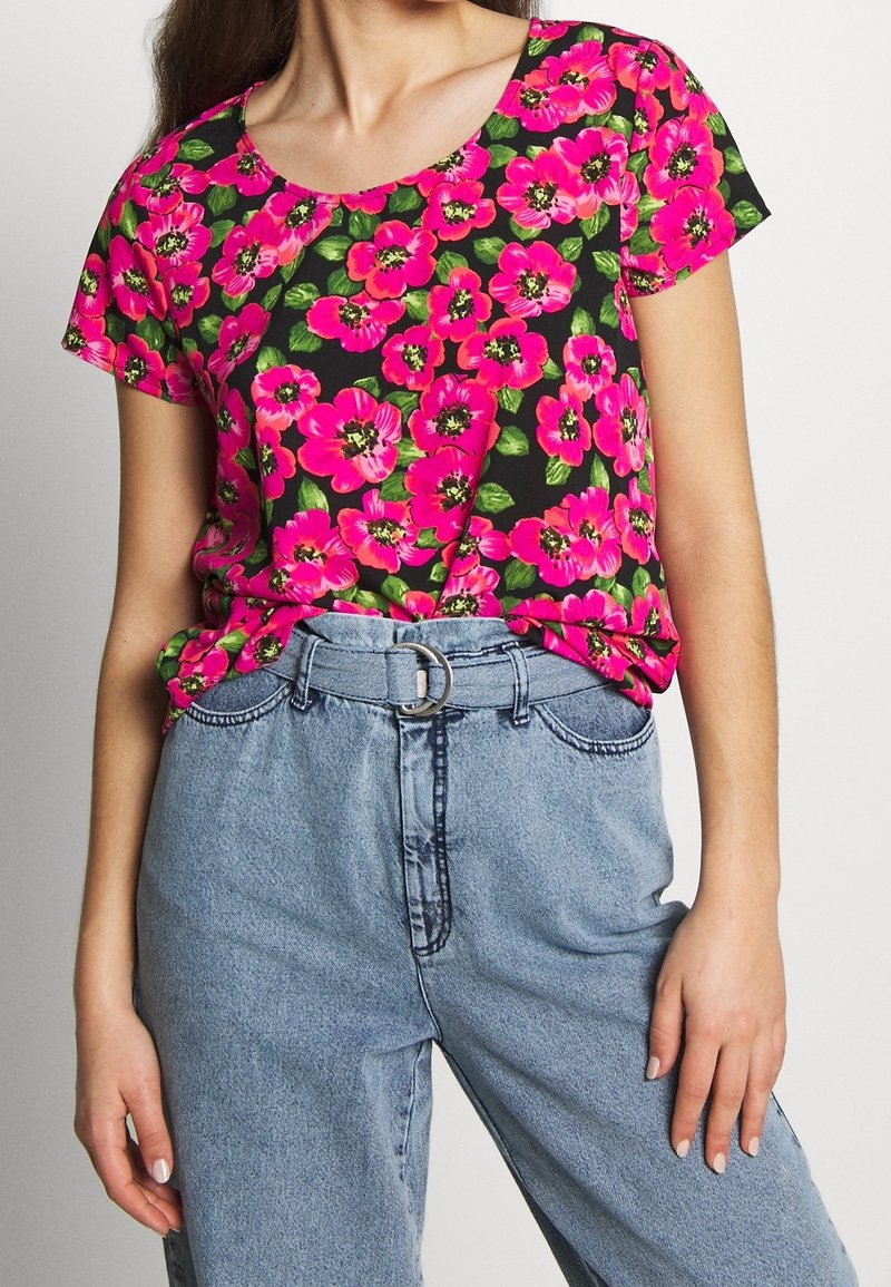 Kwiatowa bluzka z krótkim rękawem z jasnoróżowymi kwiatami na czarnym tle, zestawiona z jasnoniebieskimi dżinsami z wysokim stanem i paskiem.