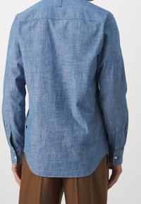 Niebieska, długosleeve koszula uszyta z lekkiego materiału. Posiada lekko zaokrąglony dół, mankiety z guzikami oraz luźny krój. Widoczny detal szycia.