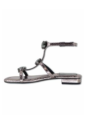 Sandalo piatto argento metallizzato con cinturino alla caviglia e tre decorazioni rotonde gioiello su sottili cinturini sopra il piede.