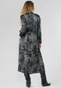 Zwarte maxi-jurk met een paisleypatroon in zilveren en gouden accenten. De stof heeft een vloeiende textuur, met lange mouwen en een getailleerde taille.