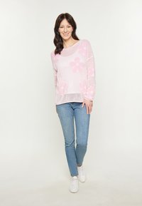 Maglione lavorato a maglia rosa chiaro con motivi floreali, vestibilità ampia, scollatura rotonda, abbinato a jeans azzurri e sneakers bianche.