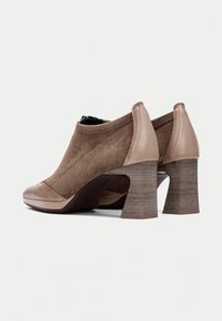 Stivali ankle in suede marrone con una punta in pelle beige lucida, tacco a blocco testurizzato e dettagli elastici alla caviglia per facilitare l'indossamento.