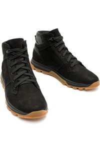 Bottines en suède noires avec des lacets noirs et des semelles en caoutchouc beige, conçues pour une utilisation en extérieur ou décontractée.