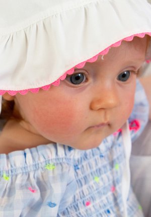 Gros plan sur un bébé portant un chapeau blanc avec une bordure rose et un vêtement bleu décoré de petits motifs colorés.