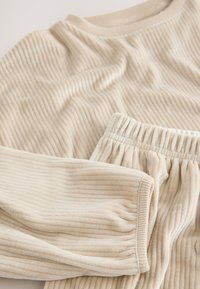 Top beige a maniche lunghe a coste e pantaloni abbinati con vita elastica, realizzati in tessuto morbido con finitura testurizzata e polsini arricciati.