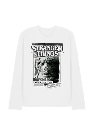 Langärmliges weißes T-Shirt mit einem schwarzen Grafikdruck. Das Design zeigt ein Monster-Gesicht und Text, der auf eine fiktive Tour in Hawkins, USA hinweist.