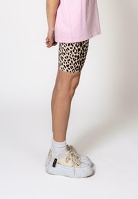 Leopard print biker shorts made of stretchy fabric, paired with white platform sneakers and knee-length socks, standing against a plain background.