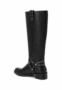 Botas de cuero negras hasta la rodilla con un acabado suave, que presentan una correa con hebilla metálica y acentos de tachuelas alrededor del tobillo. Diseño de tacón apilado.