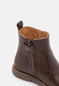 Hnědé kožené kotníkové boty se zipem na boku, poutkem na stažení, viditelným švem a vyraženým logem "bisgaard" na vnější straně.