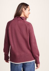 Oversized maroon knit sweater with a high collar, ribbed hem, and white side stripes, featuring a textured fabric and relaxed fit.