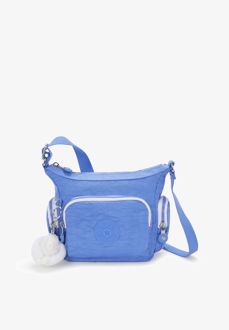 Blå nylonaxelväska med en cirkulär logotyp, vita dragkedjeaccentueringar och en fluffig nyckelring fäst. Kompakt form med justerbar rem.