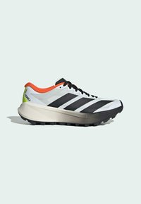 Chaussure de sport blanche avec des rayures noires, des accents orange et des lacets noirs. Présente une semelle texturée et une semelle intermédiaire grise légèrement rembourrée.