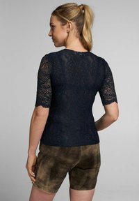 Marineblaues Spitzenoberteil mit kurzen Ärmeln, verziert mit einem Blumenmuster und gewellten Kanten, kombiniert mit braunen Wildleder-Shorts.