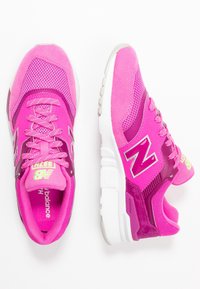 Chaussures de sport roses en mesh et suède, design texturé, logo "N" proéminent et semelle blanche amortissante. Les lacets sont assortis à la couleur des chaussures.