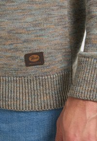 Maglione lavorato a maglia in tonalità tenui di blu, marrone e verde. Presenta un orlo a coste e una toppa in pelle marrone con dettagli del logo.