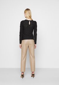 Top de renda preta de manga longa com detalhe em buraco nas costas, combinado com calças de couro bege claro. Sandálias pretas de salto alto completam o look.