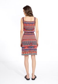 Multikleurige mouwloze jurk met complexe patronen in rood, blauw en teal. Rechte zoom en elastische tailleband voor de pasvorm.