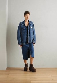 Denim jacket with two chest pockets, paired with a knee-length skirt in the same fabric, and brown ankle boots on a wooden floor.