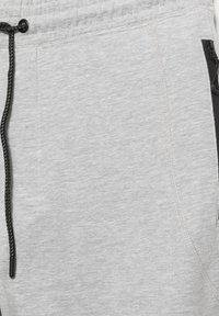 Közeli kép világosszürke melegítőnadrágról fekete zsinórral és látható varrással a szövet textúráján.