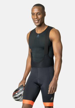 Schwarze sportliche Bib-Shorts mit orangefarbenen Akzenten, feuchtigkeitsableitendem Stoff, ärmellosem Design und gepolsterter Sattel, gehalten mit einem Helm in der Hand.