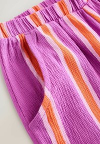 Shorts rayés violets avec une ceinture élastique, ornés de larges rayures orange et rose et un tissu texturé. Comprennent des poches latérales.