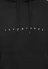 Čierna mikina s kapucňou a predným klokánkovým vreckom, s potlačou "JACK & JONES" bielymi písmenami na hrudi. Materiál z bavlnenej zmesi.