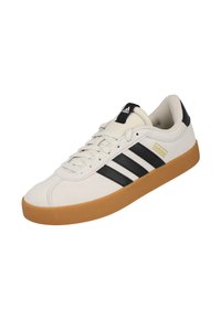 Zapatilla de ante blanca con rayas negras, suela de goma y acentos beige. Punta redonda, diseño con cordones y cuello acolchado para mayor comodidad.