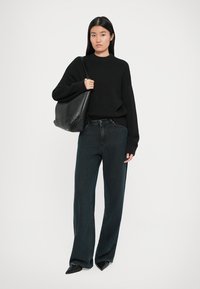 Zwarte gebreide trui, donkerblauwe hoogtijdje jeans, zwarte tas. Model draagt zwarte schoenen met puntige neuzen. Eenvoudige, ontspannen pasvorm, textuurmateriaal.