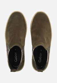 Zapatos mocasines de ante marrón con paneles laterales elásticos, suela de goma texturizada y marca interior en negro. Parte superior suave con un diseño de punta redonda.