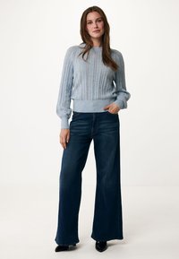 Světle modrý pletený svetr s texturovaným vzorem, kombinovaný s tmavými džínovými kalhotami s širokými nohavicemi. Svetr má žebrovaný lem a rukávy.