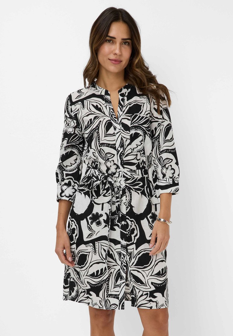 Schwarz-weiß gemustertes Kleid mit floralem Druck, Dreiviertelärmeln, kragenähnlichem Ausschnitt, tailliertem Schnitt und leichtem Stoff.