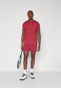 Maroon athletic t-shirt and shorts made of lightweight fabric, paired with white socks and tennis shoes, holding a tennis racket.