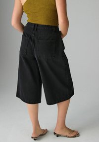 Culottes de mezclilla negra con un ajuste holgado, que cuentan con dos bolsillos traseros y un dobladillo que llega a la mitad de la pantorrilla. Llevados con sandalias minimalistas.