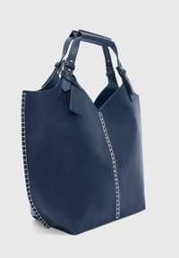 Marineblauwe leren tote bag met dubbele handvatten, voorzien van een contrasterende stikselafwerking langs de naden en een labelaccent aan één handvat.