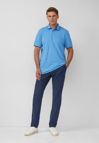 Light blue polo shirt with a contrasting navy collar and sleeves, paired with navy pants and white sneakers, set against a plain background.