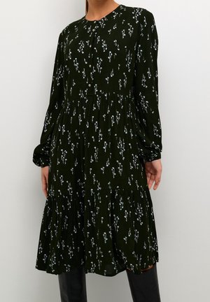 Woman wearing a long-sleeve, black midi dress with small white floral prints and buttons down the front, paired with black boots.
