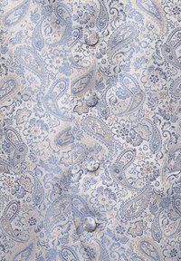 Hellblauem Stoff mit kunstvollen Paisley- und Blumenmustern, verziert mit goldenen Akzenten. Zwei Knöpfe auf der linken Seite sichtbar.